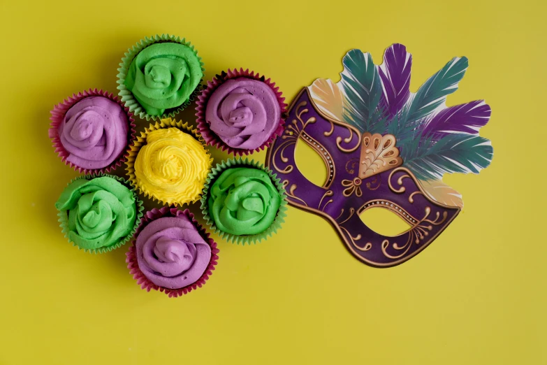 a mardi gras mask and cupcakes on a yellow background, inspired by Mardi Barrie, trending on pexels, background image, complementary colour scheme, purple green color scheme, complementary color scheme