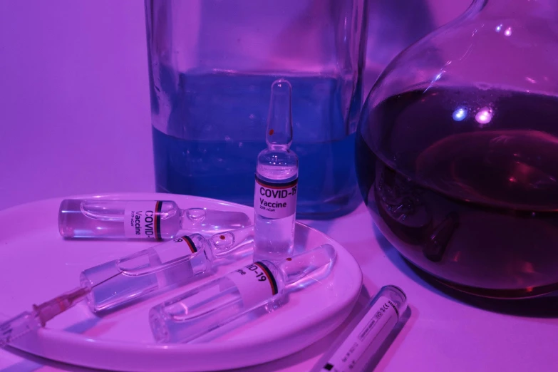 a white plate topped with a glass filled with liquid, an album cover, by Jeanna bauck, pexels contest winner, vibrant vials, purple and blue neon, syringe, medical labels