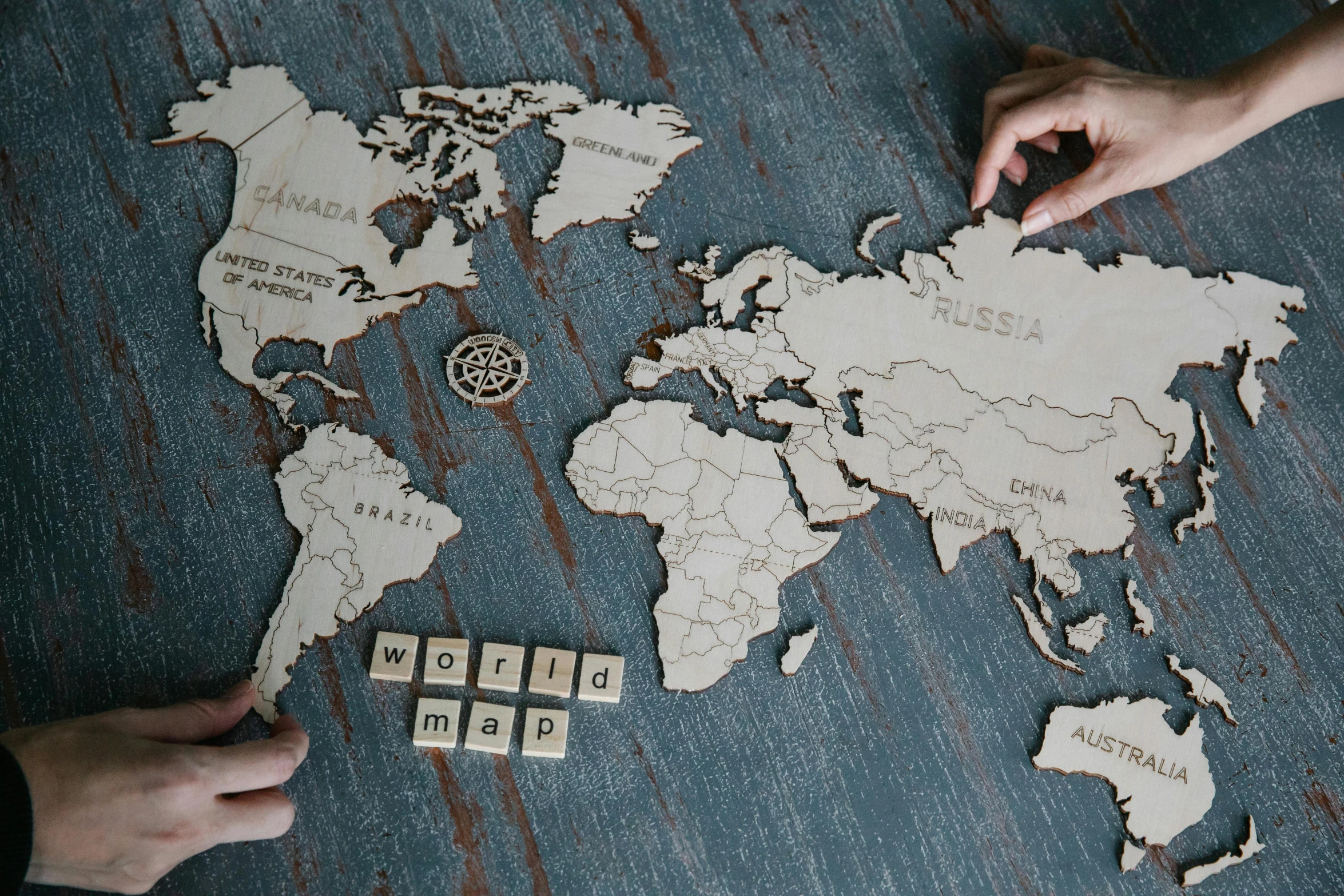 a person sitting at a table with a map of the world on it, a jigsaw puzzle, trending on unsplash, interactive art, wooden art toys on base, with names, wood burn, alex heywood