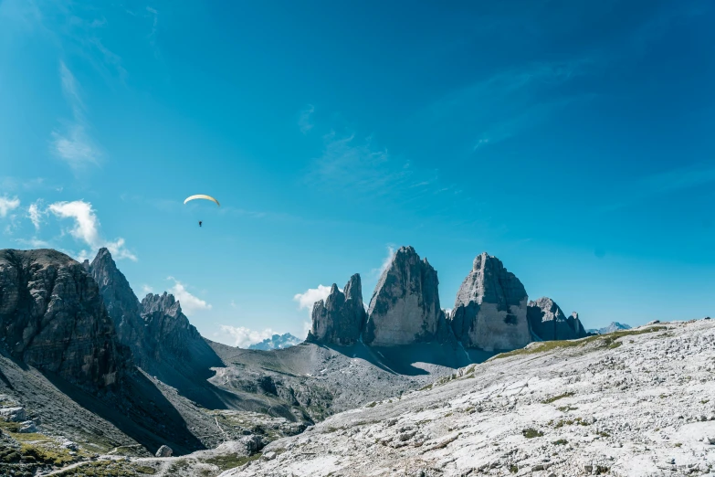 a paraglider flying over the mountains on a sunny day, by Carlo Martini, pexels contest winner, tall stone spires, fine art print, gondolas, chalk cliffs above