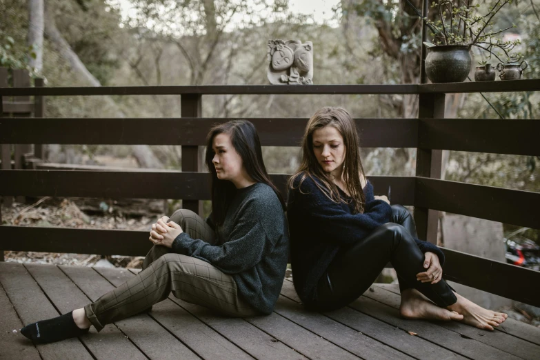 a couple of women sitting on top of a wooden deck, a portrait, unsplash, portrait image, concerned, in a cabin, sitting on the ground