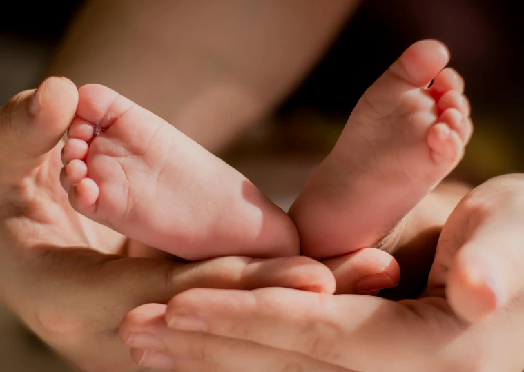 a close up of a person holding a baby's feet, incoherents, laying down, different sizes, warm coloured, no watermarks