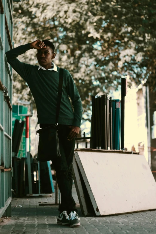 a man standing on a sidewalk next to a building, wearing a green sweater, black teenage boy, thinking pose, mechanics