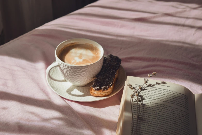 an open book sitting on top of a bed next to a cup of coffee, by Lucia Peka, trending on unsplash, romanticism, white and pink cloth, having a snack, black, sparkling in the sunlight