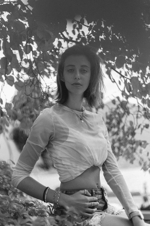 a black and white photo of a woman leaning against a tree, inspired by Maud Naftel, antipodeans, wearing a crop top, natalia dyer, helene frankenthaler, billy butcher