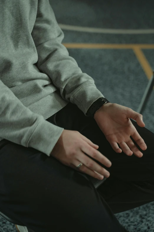 a man sitting on a chair with his hands on his knees, trending on unsplash, wearing two silver bracelets, wearing sweatshirt, slight haze, leather cuffs around wrists