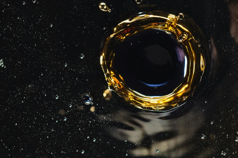 a glass filled with liquid sitting on top of a table, an album cover, by Julia Pishtar, trending on unsplash, process art, ornate galactic gold, black hole in space, whisky, olive oil