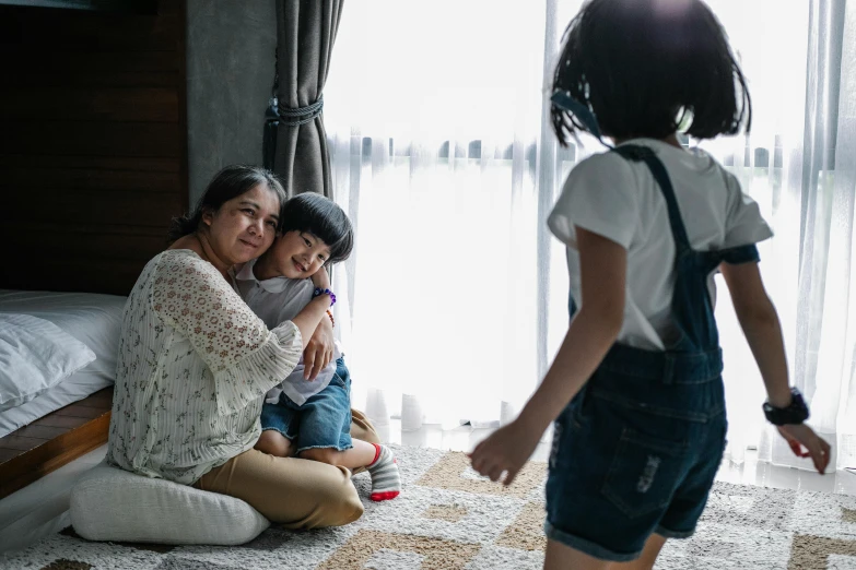 a woman sitting on the floor next to a little girl, pexels contest winner, husband wife and son, standing in corner of room, young asian girl, looking outside