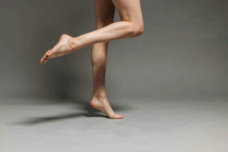 a woman holding a tennis racquet in one hand and a tennis racquet in the other, inspired by Elizabeth Polunin, unsplash, arabesque, bare leg, on grey background, feet, dancing on a pole
