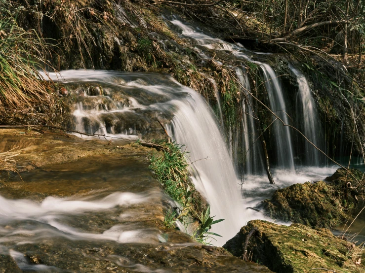 a small waterfall flowing through a lush green forest, an album cover, by Mirko Rački, unsplash contest winner, hurufiyya, flowing clear water creek bed, medium format. soft light, thumbnail, brown