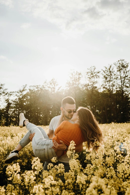 a man holding a woman in a field of flowers, by Niko Henrichon, pexels contest winner, sitting on the ground, yellow hue, instagram story, backlight