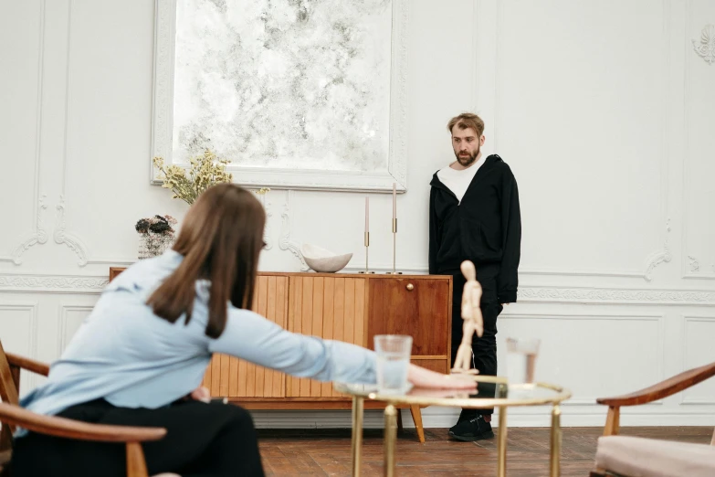 a man standing next to a woman in a living room, by Emma Andijewska, visual art, on a white table, set design, holding court, product introduction photo