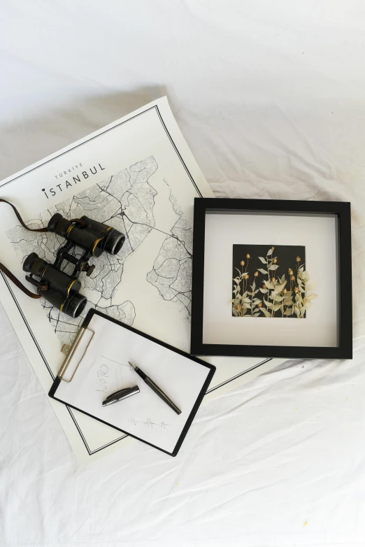 a pair of binoculars sitting on top of a bed, a picture, by Nazmi Ziya Güran, unsplash contest winner, modern european ink painting, golden leaves at frame border, cartography map art, square pictureframes, dwell