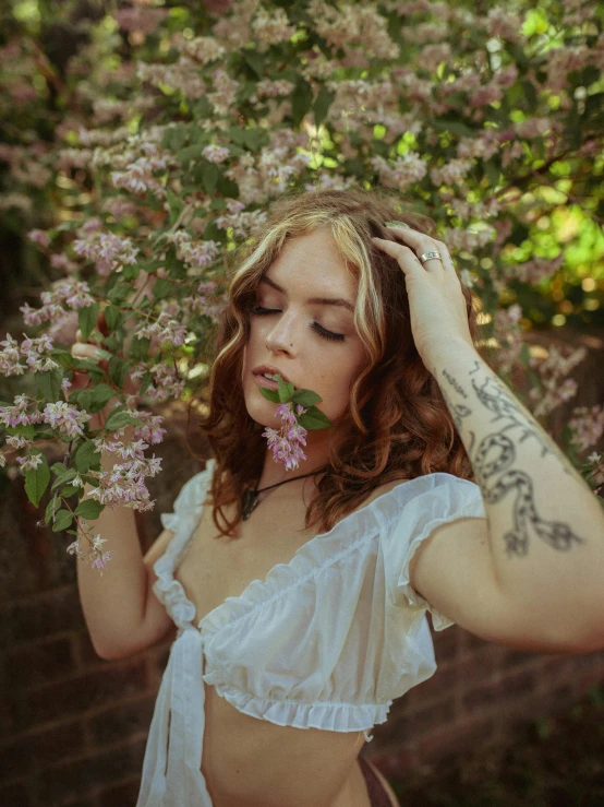 a woman standing in front of a bush with flowers, inspired by Elsa Bleda, trending on pexels, renaissance, with tattoos, sydney sweeney, lilac, medium format