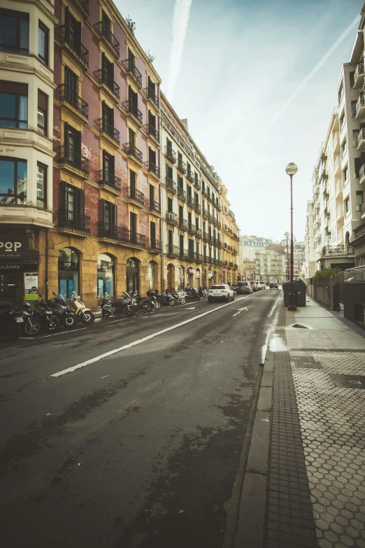 a city street filled with lots of tall buildings, a picture, inspired by Tomàs Barceló, pexels contest winner, baroque, one motorbike in center of frame, sparsely populated, spain, square