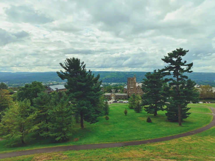 a couple of trees sitting on top of a lush green field, a colorized photo, unsplash, renaissance, cornell, overlooking a valley, holy cross, building in the distance