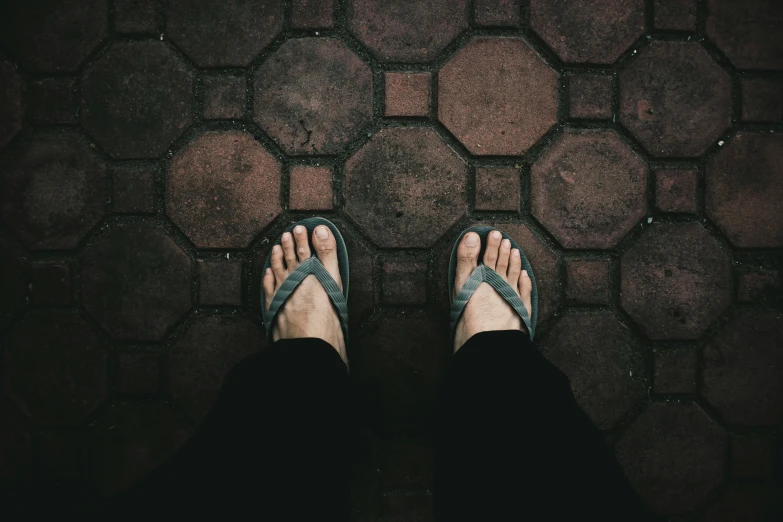 the feet of a person standing on a tiled floor, pexels contest winner, flip flops, grey clothes, standing in a dark, outside on the ground