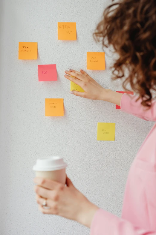 a woman standing in front of a wall covered in post it notes, product view, pink and orange, woman drinking coffee, game