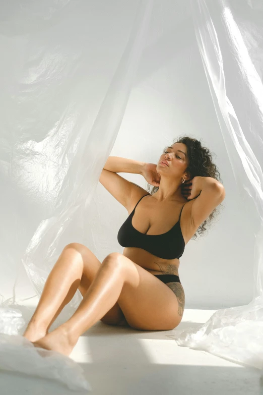 a woman in a black bikini sitting on a bed, sun overhead, soft twirls curls and curves, promo image, curvy build