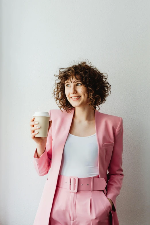 a woman in a pink suit holding a cup of coffee, trending on pexels, curly brown hair, aussie baristas, professional profile picture, samma van klaarbergen