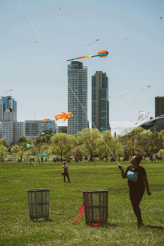 a group of people flying kites in a park, winnipeg skyline, melbourne, tall buildings, toronto