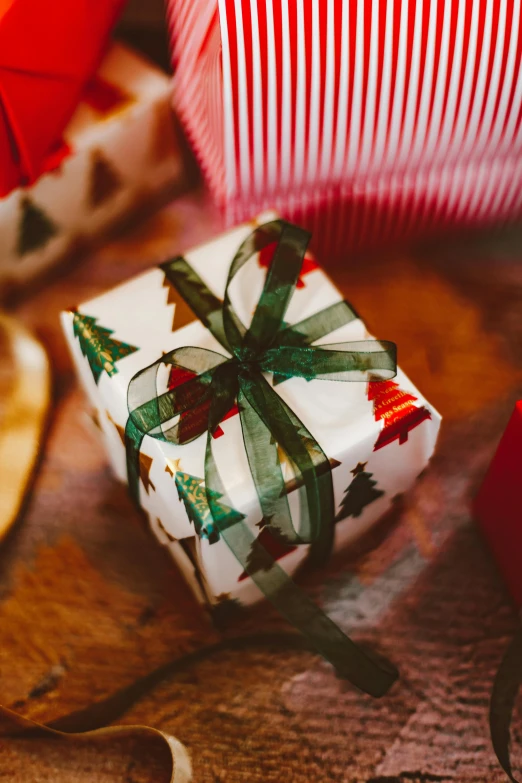 a christmas present sitting on top of a wooden table, pexels, happening, square, ribbons, close - up photograph, gif