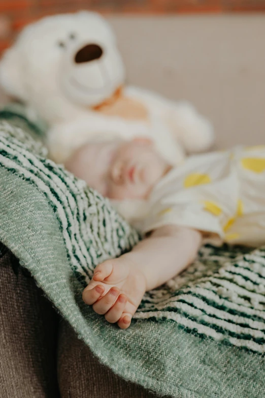 a baby sleeping on a couch next to a teddy bear, by Alice Mason, pexels contest winner, symbolism, close up portrait shot, covered with blanket, mini model, lachlan bailey