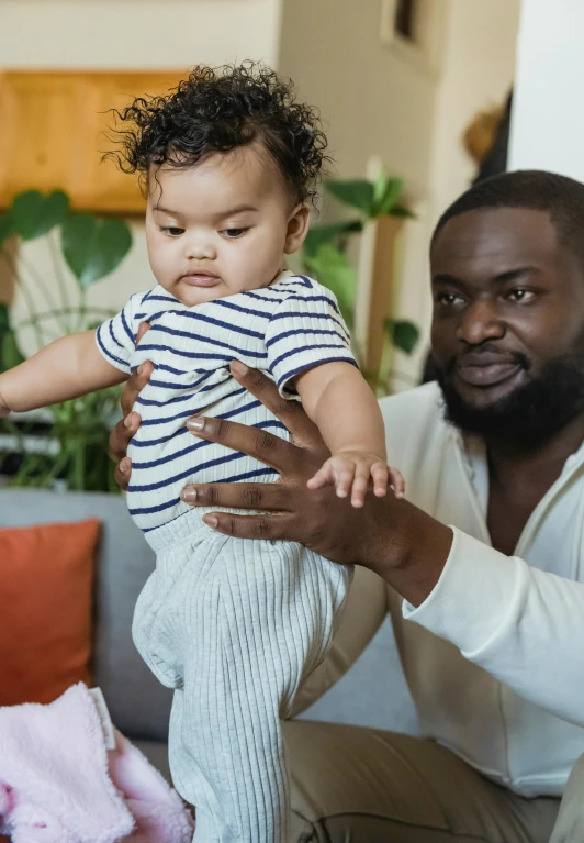 a man holding a baby while sitting on a couch, diverse, dancing with each other, thumbnail, trending
