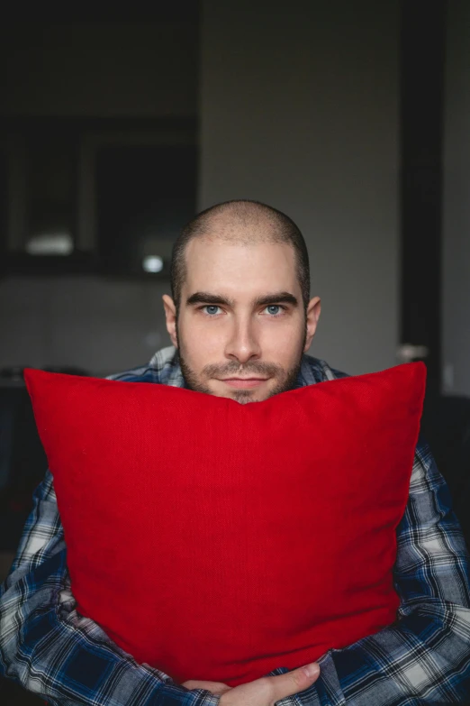 a man sitting on a couch holding a red pillow, by Adam Marczyński, pexels contest winner, square masculine facial features, buzz cut, loving stare, h3h3