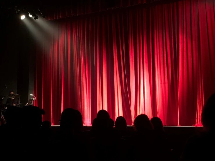 a man standing on a stage in front of a red curtain, pexels contest winner, some people are sitting, from the distance, standup, pitch black room