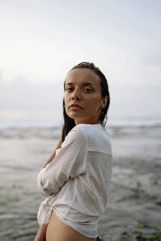 a woman standing on top of a beach next to the ocean, a portrait, unsplash, renaissance, dafne keen, wearing a linen shirt, bali, dewy skin