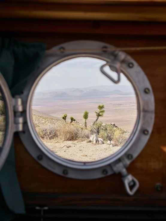 a round mirror sitting on top of a wooden table, a picture, inside large window of ship, mojave desert, slide show, shot with sony alpha