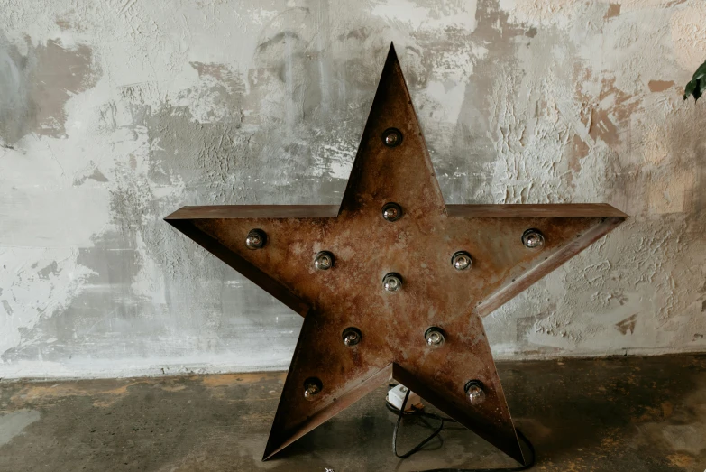 a rusty metal star sitting on top of a cement floor, by Nick Fudge, unsplash, kinetic art, large led lights, vintage inspired, marquee, full front view