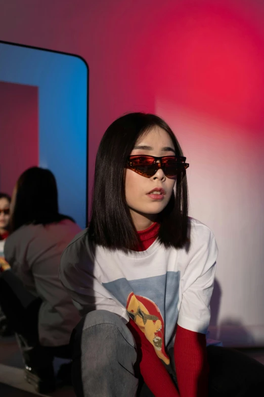 a woman sitting on a bench in front of a mirror, an album cover, inspired by Yanjun Cheng, trending on pexels, red sunglasses, futuristic fashion show, asian human, graphic tees