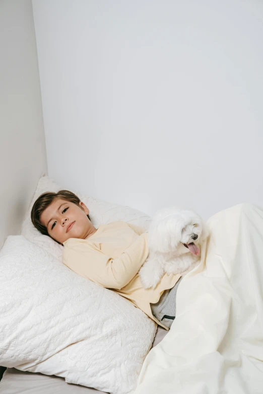 a woman laying in bed with a white dog, wearing nanotech honeycomb robe, teen boy, light cream and white colors, profile image