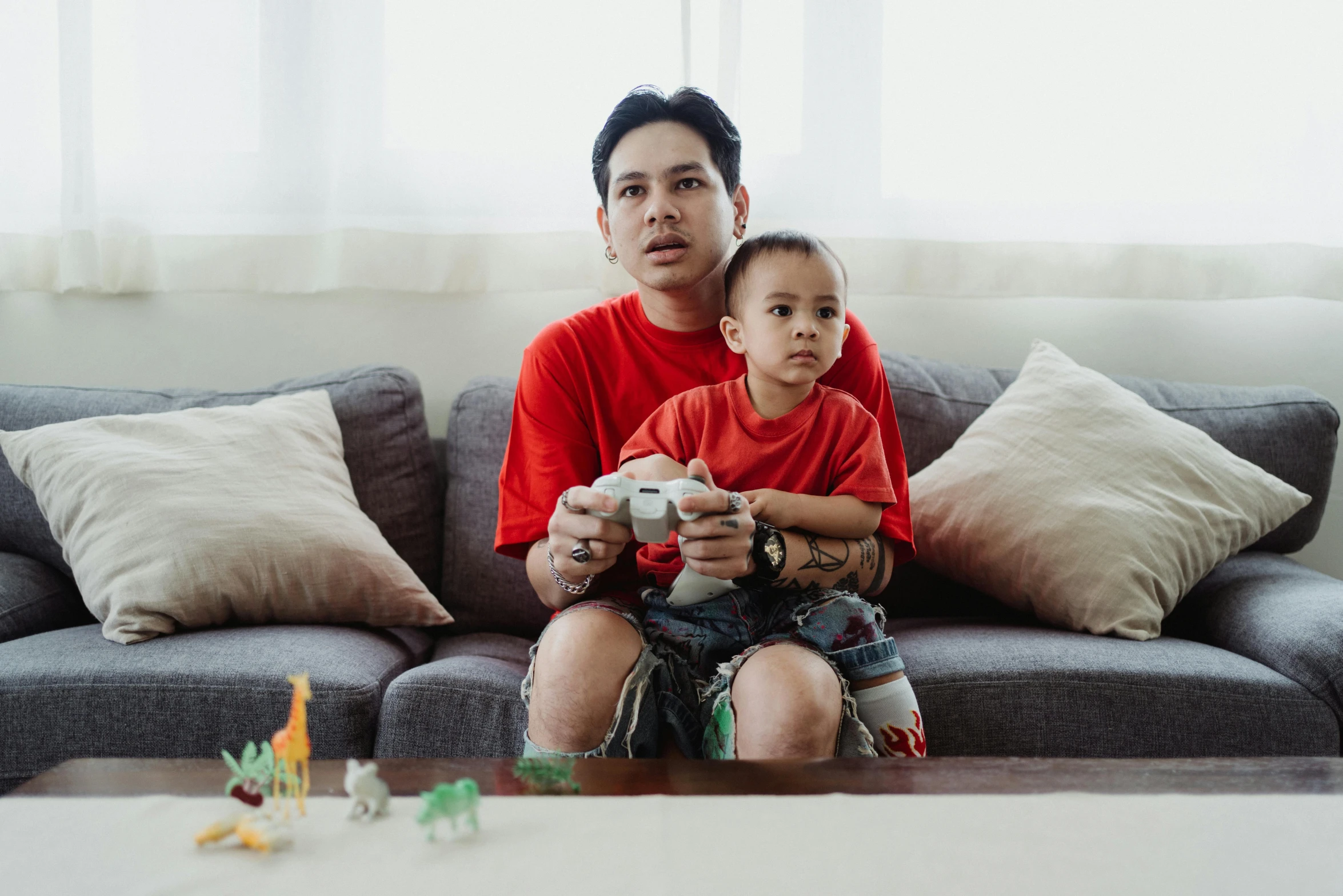 a man sitting on top of a couch holding a child, pexels contest winner, video game control, avatar image, asian man, toy photo