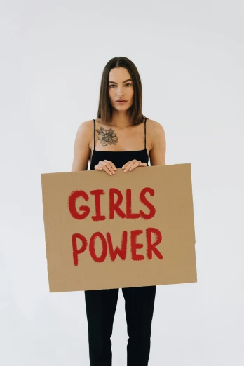 a woman holding a sign that says girls power, trending on pexels, sasha grey, show, tattooed, profile image