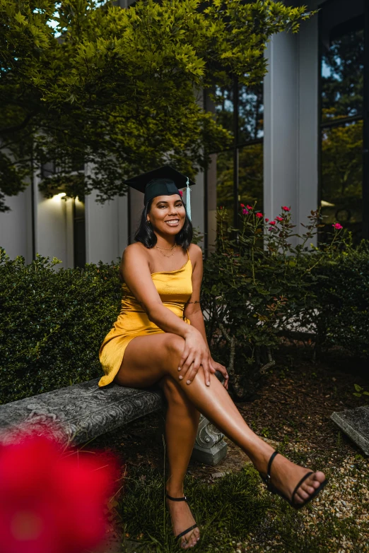 a woman in a yellow dress sitting on a bench, a portrait, unsplash, graduation photo, photo of a black woman, sitting on a stool, bushes in the background