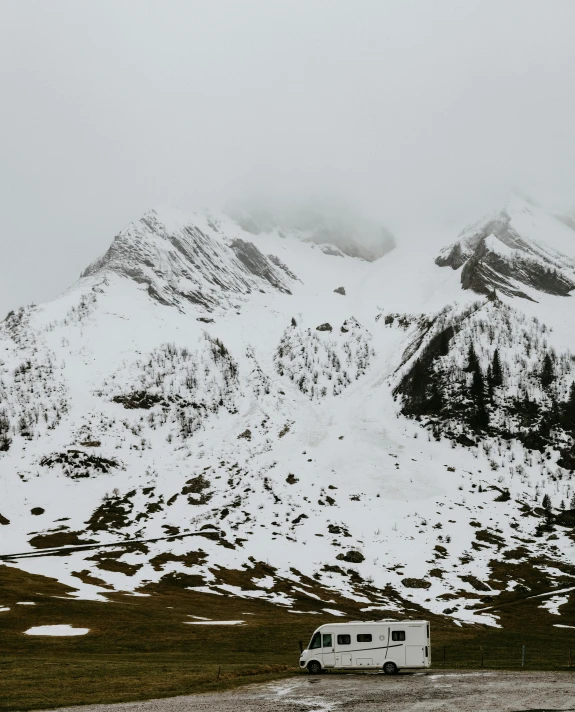 a van parked in front of a snowy mountain, by Johannes Voss, pexels contest winner, renaissance, white fog painting, snow on the body, high quality photo, overcast gray skies