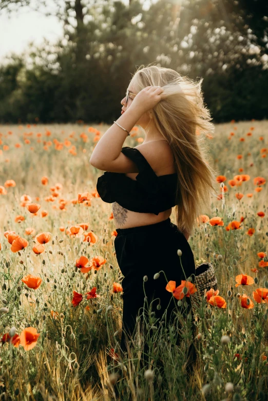 a woman standing in a field of flowers, by Zofia Stryjenska, pexels contest winner, wearing a black cropped tank top, instagram post, beautiful blonde hair, orange and black tones