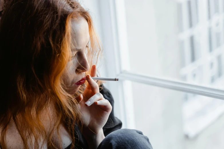 a woman smoking a cigarette in front of a window, trending on pexels, thin long auburn hair, hr ginger, depressed, profile image