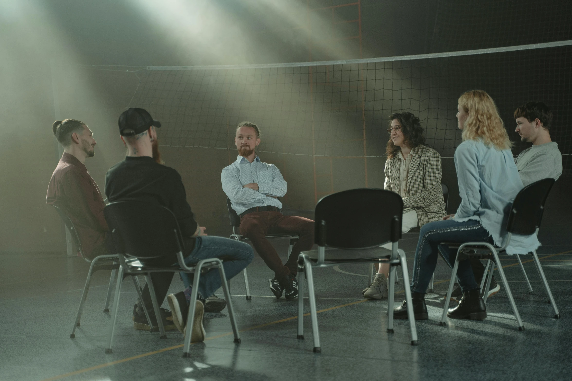 a group of people sitting in chairs in a room, in the middle of an empty room