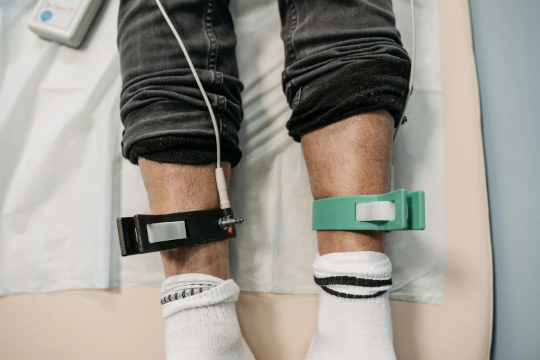 a close up of a person in a hospital bed, a colorized photo, by Adam Marczyński, trending on pexels, foot wraps, green and black, pair of keycards on table, connected to wires