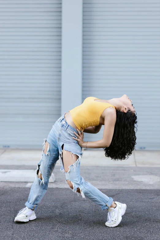 a woman in ripped jeans is dancing on the street, trending on pexels, arabesque, wearing yellow croptop, curly, pose 4 of 1 6, woman with black hair