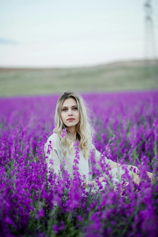 a woman sitting in a field of purple flowers, inspired by Elsa Bleda, pexels contest winner, color field, blonde women, salvia, white, low quality photo