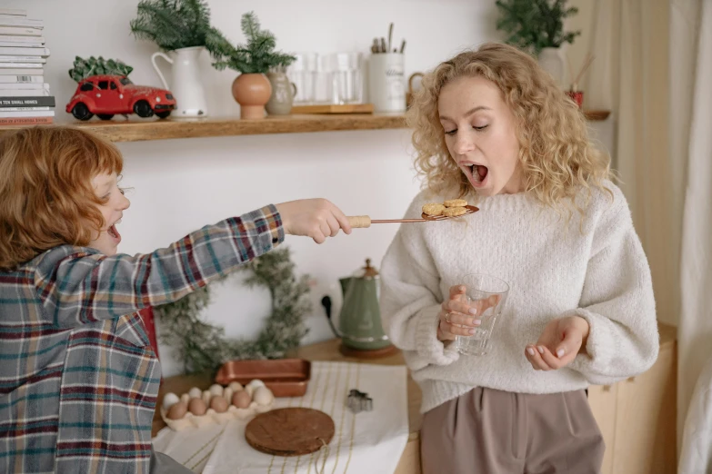 a couple of women standing next to each other in a kitchen, by Emma Andijewska, pexels contest winner, eating garlic bread, kids playing, spatula, holiday