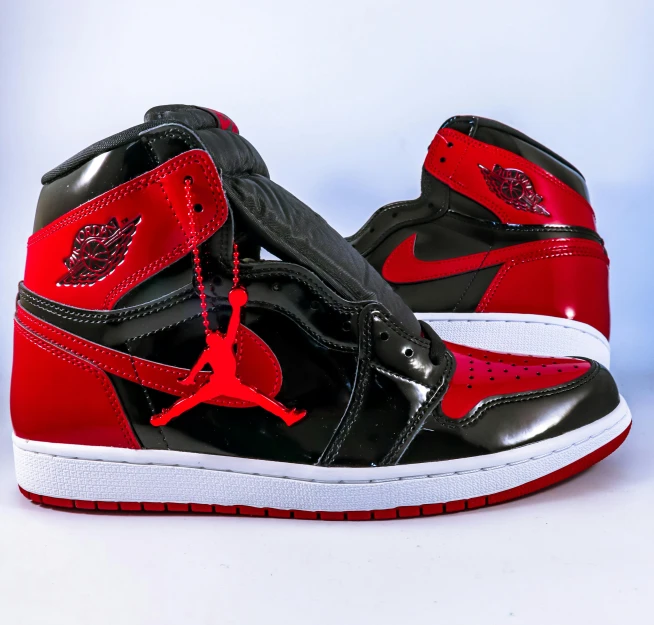 a pair of black and red sneakers on a white surface, inspired by Jordan Grimmer, pexels, hyperrealism, patent leather, air jordan 1 high, front top side view, metallic red