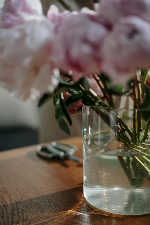 a vase filled with pink flowers on top of a wooden table, a still life, unsplash, low detail, clear glass, indoor picture, upclose