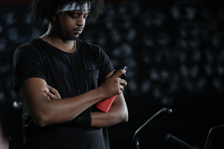 a man looking at his cell phone while standing in a gym, a portrait, trending on pexels, process art, red sweatband, a black man with long curly hair, dark. no text, bandage on arms