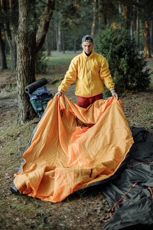 a man standing next to a tarp in the woods, dark grey and orange colours, inflatable, multi-part, gray